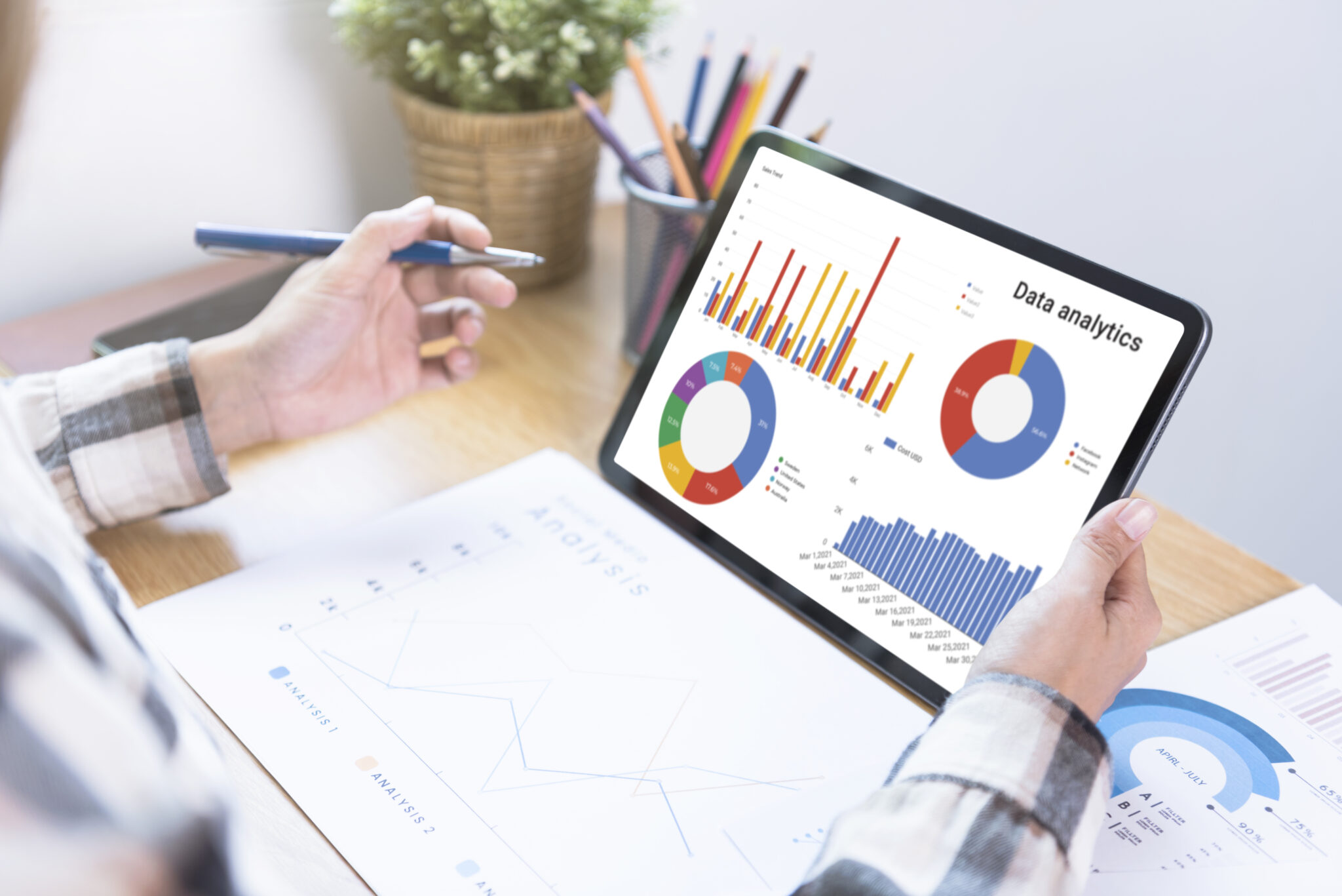 An SEO Manager analyzing a website performance's data analytics charts on a tablet, with printed search traffic graphs on the desk