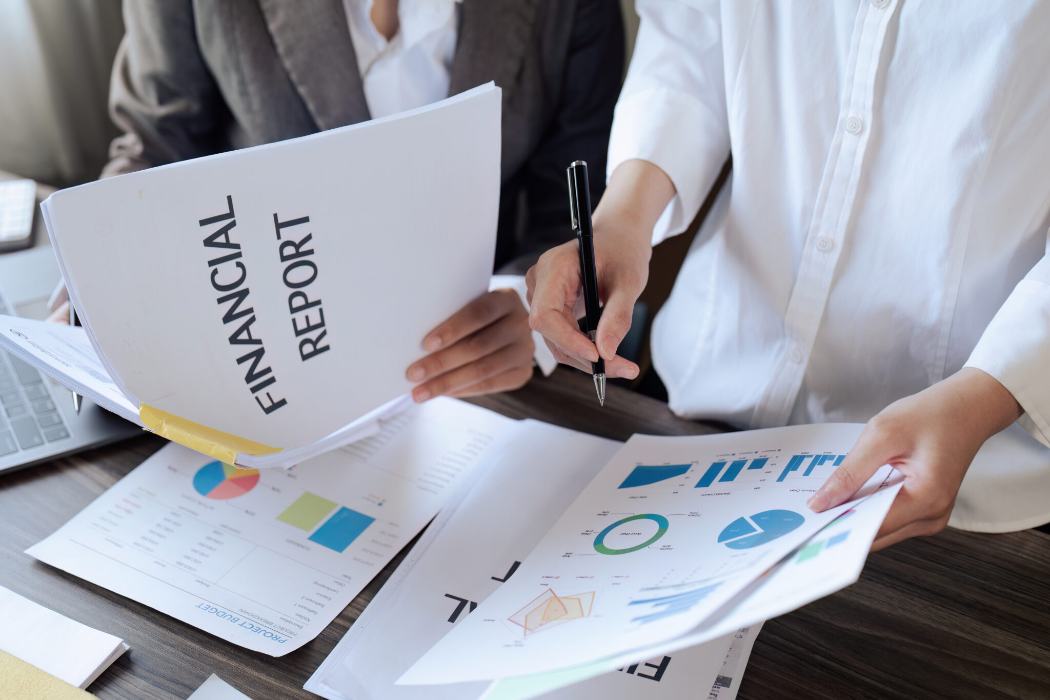 Close-up of a senior manager and employee discussing project budget, holding a financial report with charts and graphs