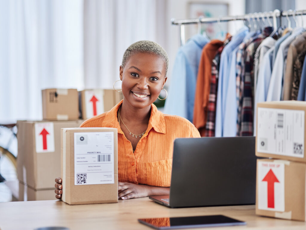 Female business owner preparing orders with a smile, balancing online sales and reputation, as clothes and packages fill the workspace