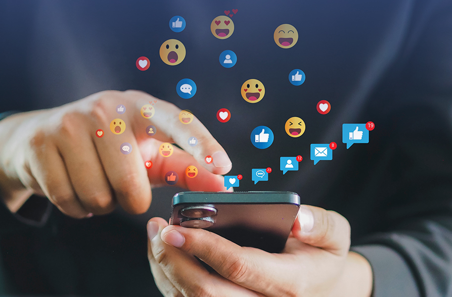 Person using a smartphone with floating social media icons and emojis above. Perfect for illustrating the concept of growing social media reach