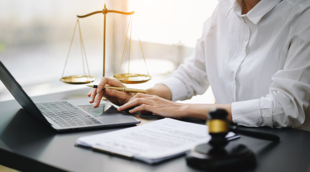 A woman in a white shirt sits at a desk with a laptop and a scale of justice, symbolizing legal content marketing