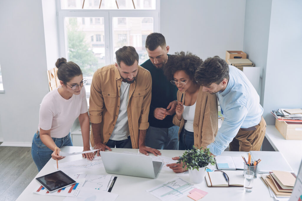 A diverse group of individuals collaborating around a laptop, representing Excell Digital Marketing Services