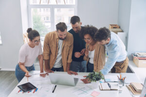 A diverse group of individuals collaborating around a laptop, representing Excell Digital Marketing Services