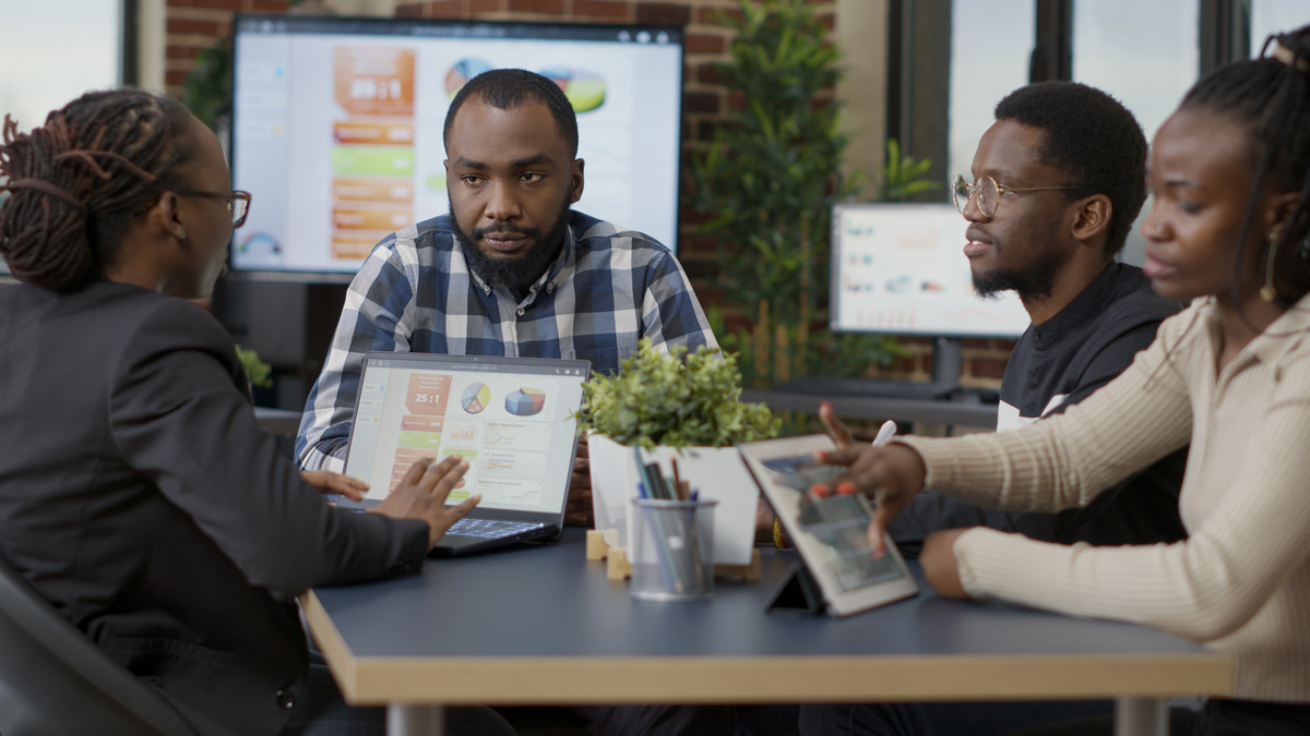 Three individuals engaged in digital marketing discussions at a table, each using a laptop, amidst a recession