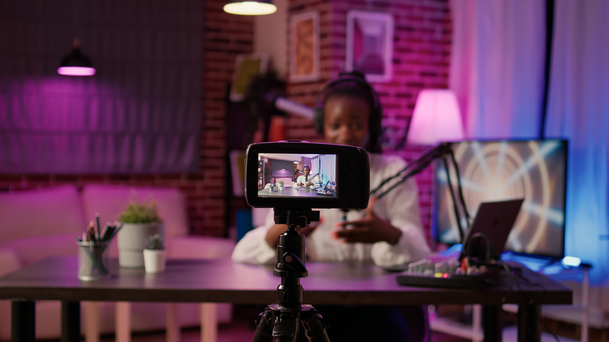 A woman sits at a table with a camera, preparing for a video shoot or content creation