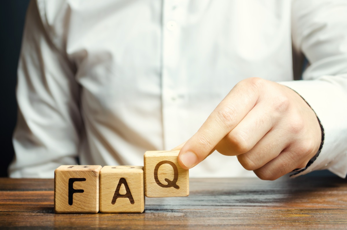 A man points to wooden blocks labeled 'FAQ', indicating a focus on frequently asked questions.