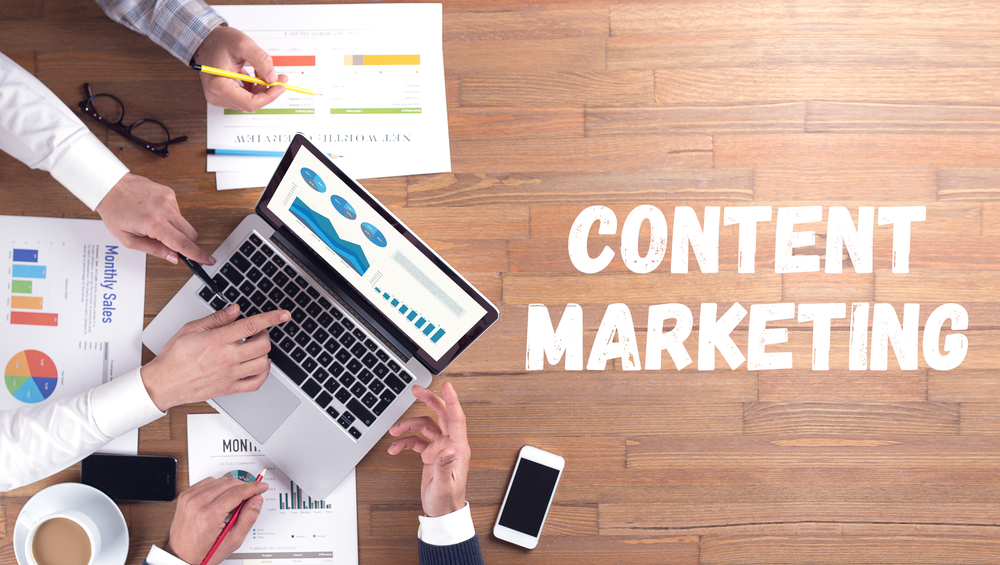 Content marketing strategy meeting with team analyzing data charts on laptop, reports, and smartphone on wooden desk for digital marketing planning