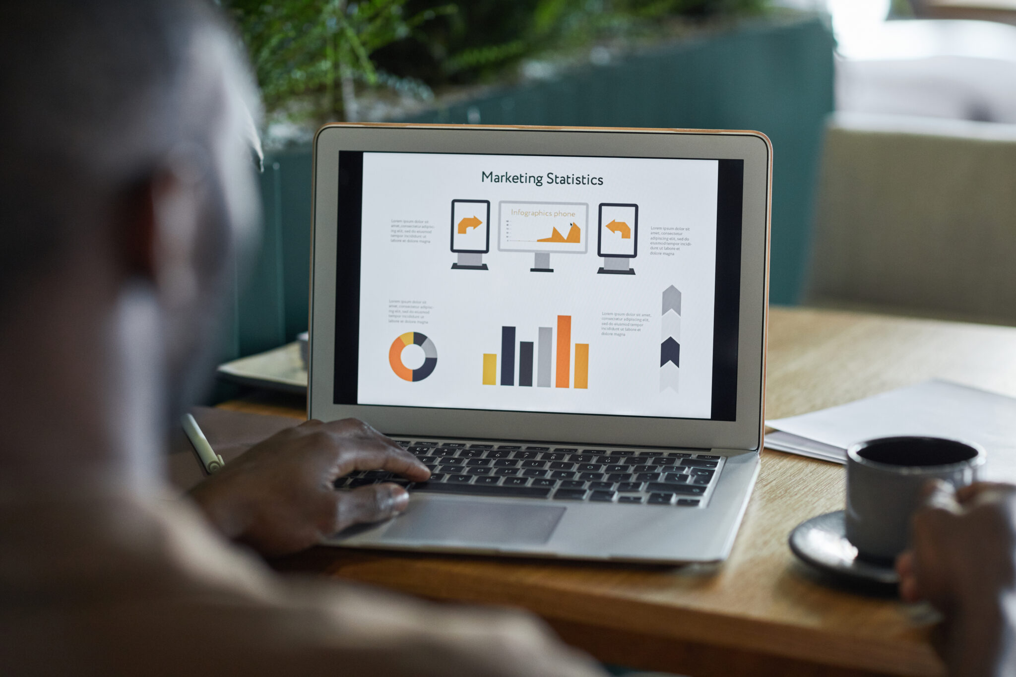 Marketing manager viewing marketing statistics from email marketing campaigns on a laptop screen while drinking coffee