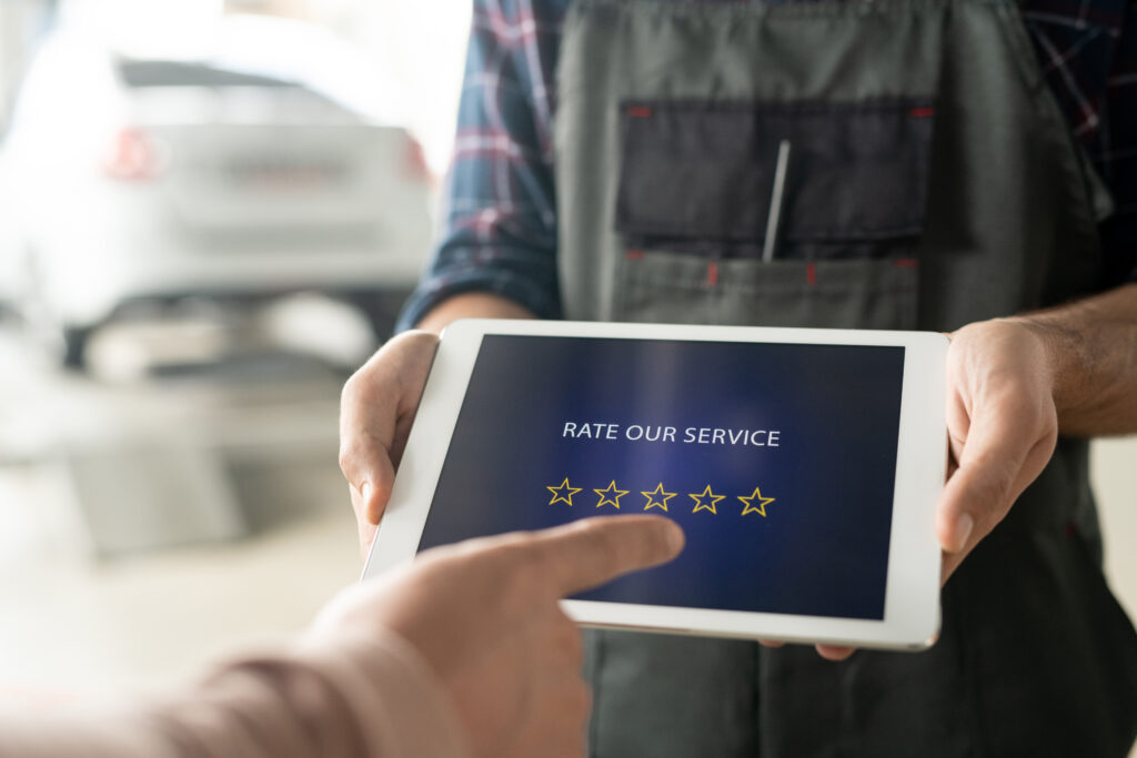 A mechanic hands over a tablet with a customer satisfaction survey, inviting clients to rate their service in a clean automotive shop