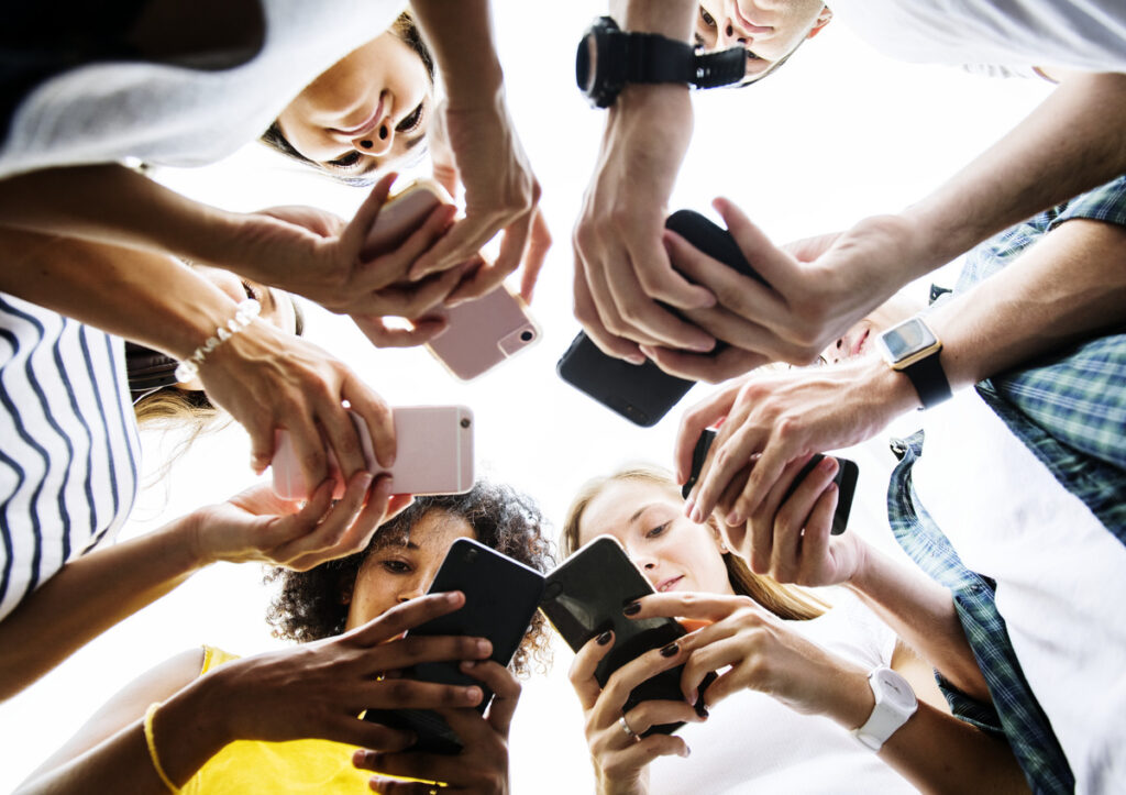 A diverse group of individuals raising their cell phones, symbolizing 2023 social media marketing trends and engagement
