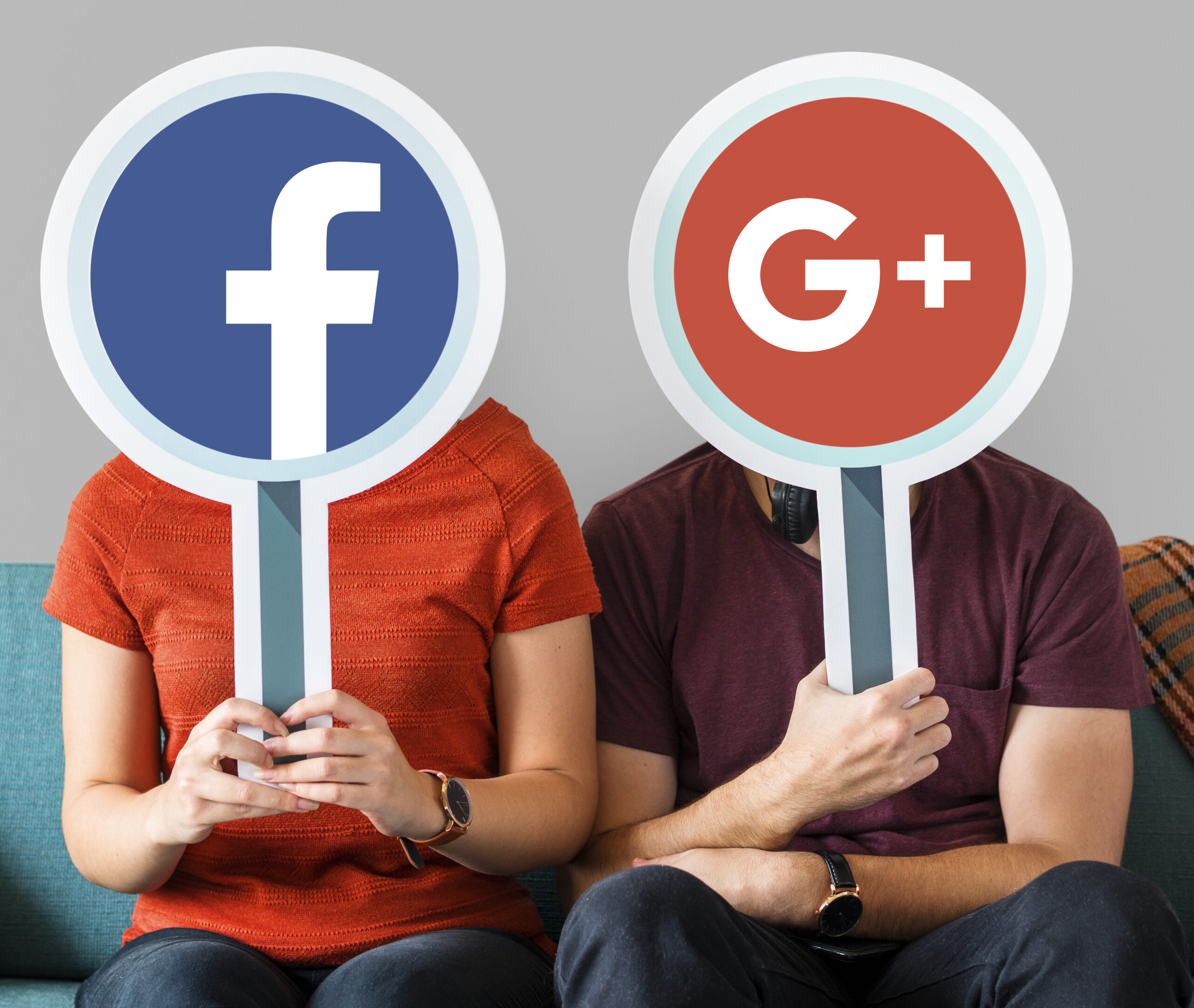 Two individuals sitting on a couch, covering their faces with circular signs showing the logos for Facebook (blue 'f') and the now-defunct Google+ (red 'G+')