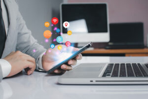 Person in a business suit using a mobile phone at a desk with a laptop, showing glowing icons for WiFi, mail, home, and shopping