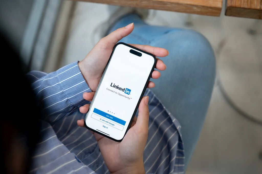 Professional using the LinkedIn app on a smartphone for career networking and job searching, representing B2B marketing and social media for business