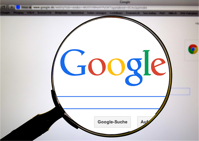 A magnifying glass held over a computer screen displaying the Google search homepage and search bar. The image symbolizes search engine optimization, digital marketing research, and online information discovery