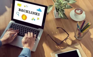 Person working on laptop with “backlinks” concept on screen, alongside coffee, notebook, and office items, representing SEO link building and digital marketing strategy