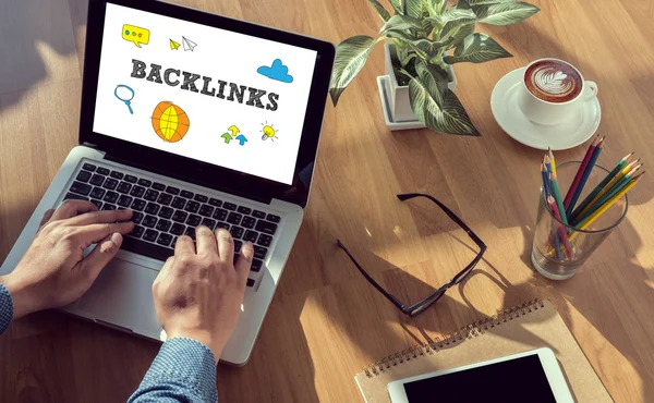 Person working on laptop with “backlinks” concept on screen, alongside coffee, notebook, and office items, representing SEO link building and digital marketing strategy