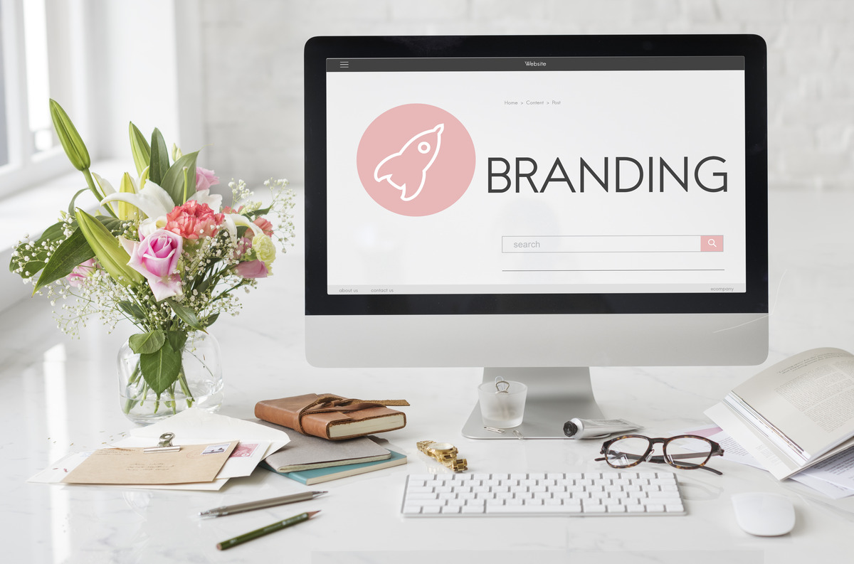 Branding concept on desktop computer screen with workspace setup, flowers, notebook, and office items, representing brand identity, design, and creative business strategy
