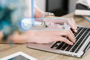 Person typing on a laptop with a digital search bar overlay, representing online search, search engine optimization (SEO), keyword research, search intent, and improving website visibility in search results.