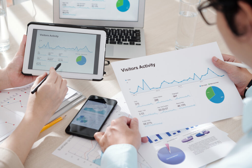 Close-up of a web traffic analysis meeting showing a user activity report with line graphs, pie charts, and data dashboards across multiple devices.